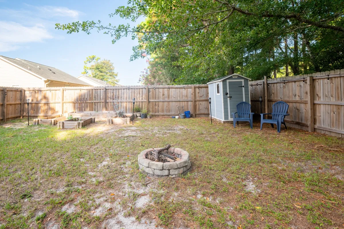 This exterior shot highlights a fire pit surrounded by blue chairs on a green lawn, with a shed and a fully fenced yard clearly visible. The setup emphasizes a welcoming, secure environment ideal for gatherings and outdoor fun, while the fence signals pet-friendliness.