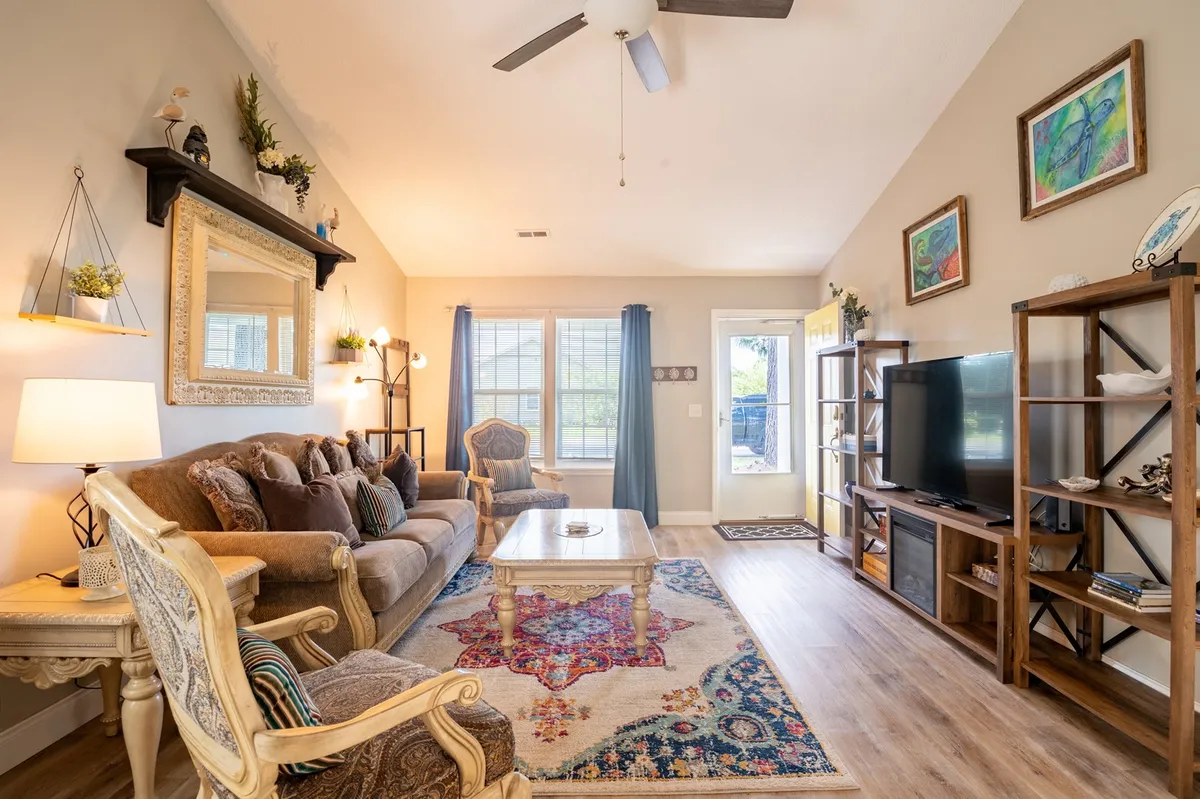 A spacious, comfortably furnished living room with a soft sofa, an inviting colorful rug, a stylish mirror, and a TV unit. The setup encourages relaxation and social activities like game nights after a day of exploring local attractions.