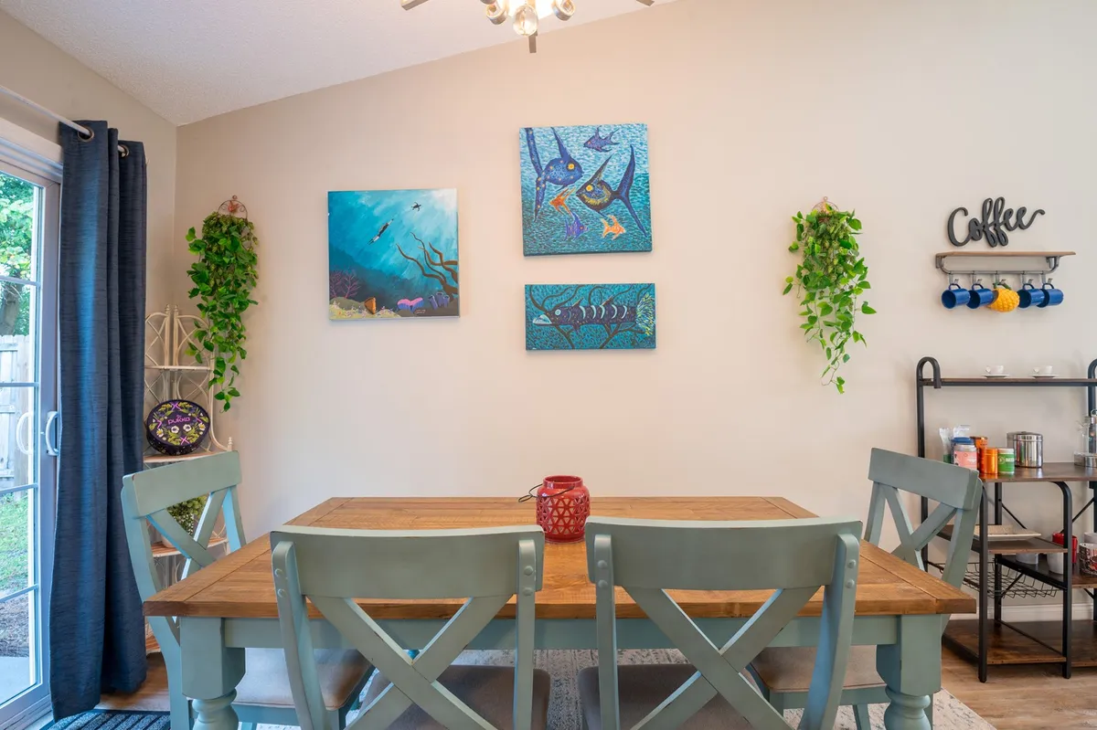 A bright, welcoming dining area featuring a large table surrounded by chairs, colorful wall art, and lush green plants. The coffee station along the wall adds a touch of convenience, suggesting a perfect spot for fueling up before a day of exploration.
