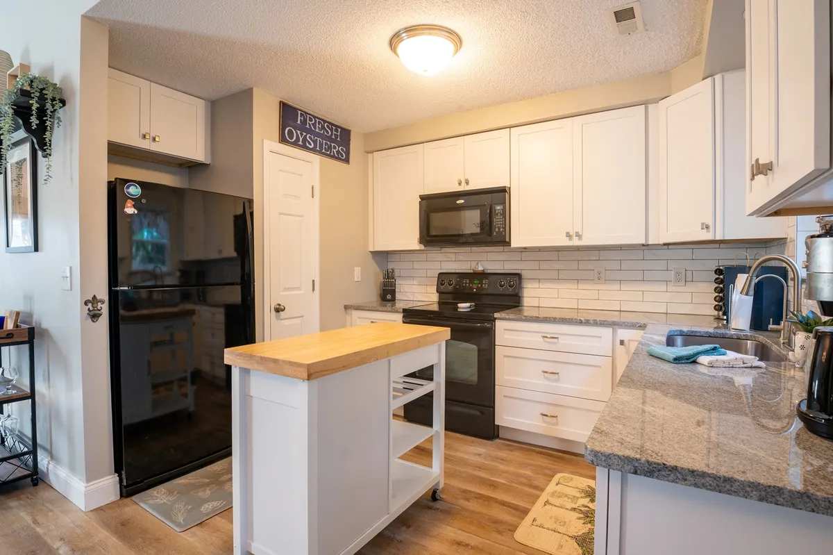 A stylish kitchen with granite countertops, black appliances, white cabinetry, and a central wooden island. The space is designed for meal preparation and gatherings, suggesting a welcoming area to cook, dine, or entertain.