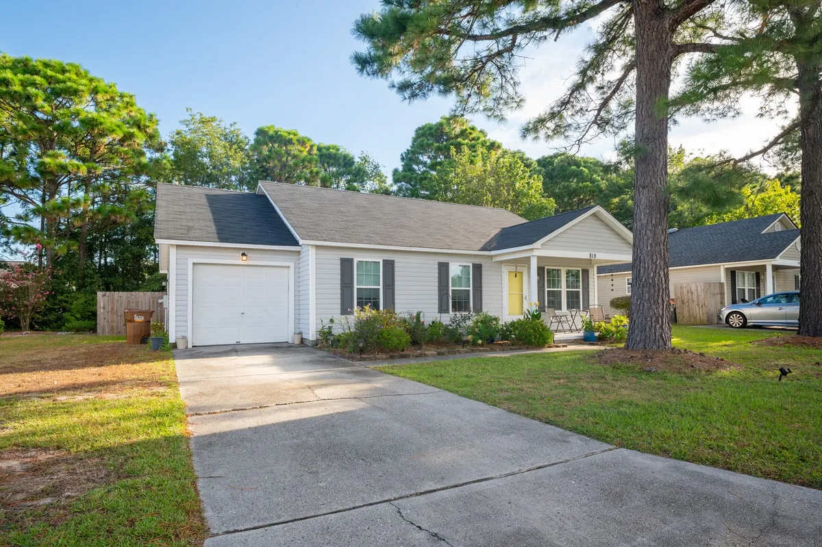 This image shows the exterior front porch of the home, featuring a welcoming yellow door, manicured lawn, and the private driveway leading up to the house. The garage is partially visible, emphasizing ease of arrival and secure parking options.