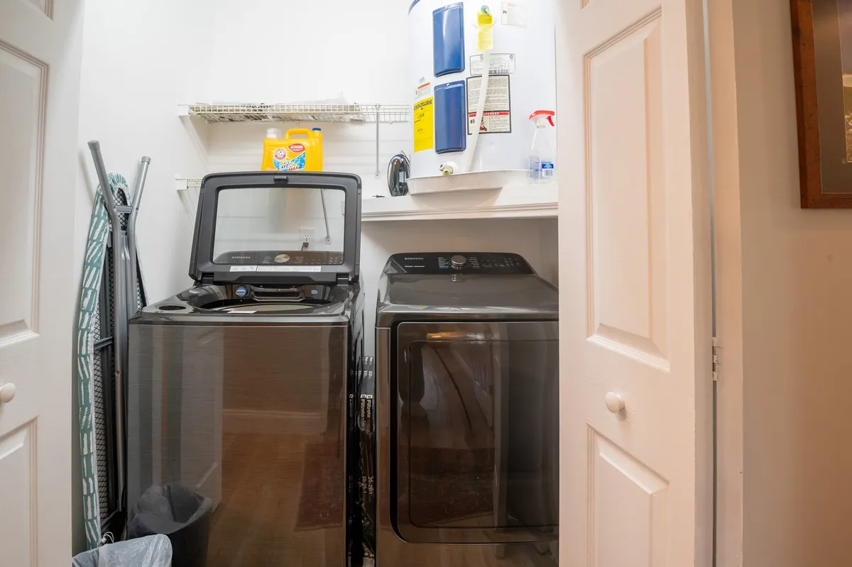 A practical interior shot focused on the laundry closet, showcasing a washer, dryer, shelf, and cleaning supplies. The space is organized and inviting, making it easy for guests to handle laundry during an extended stay.
